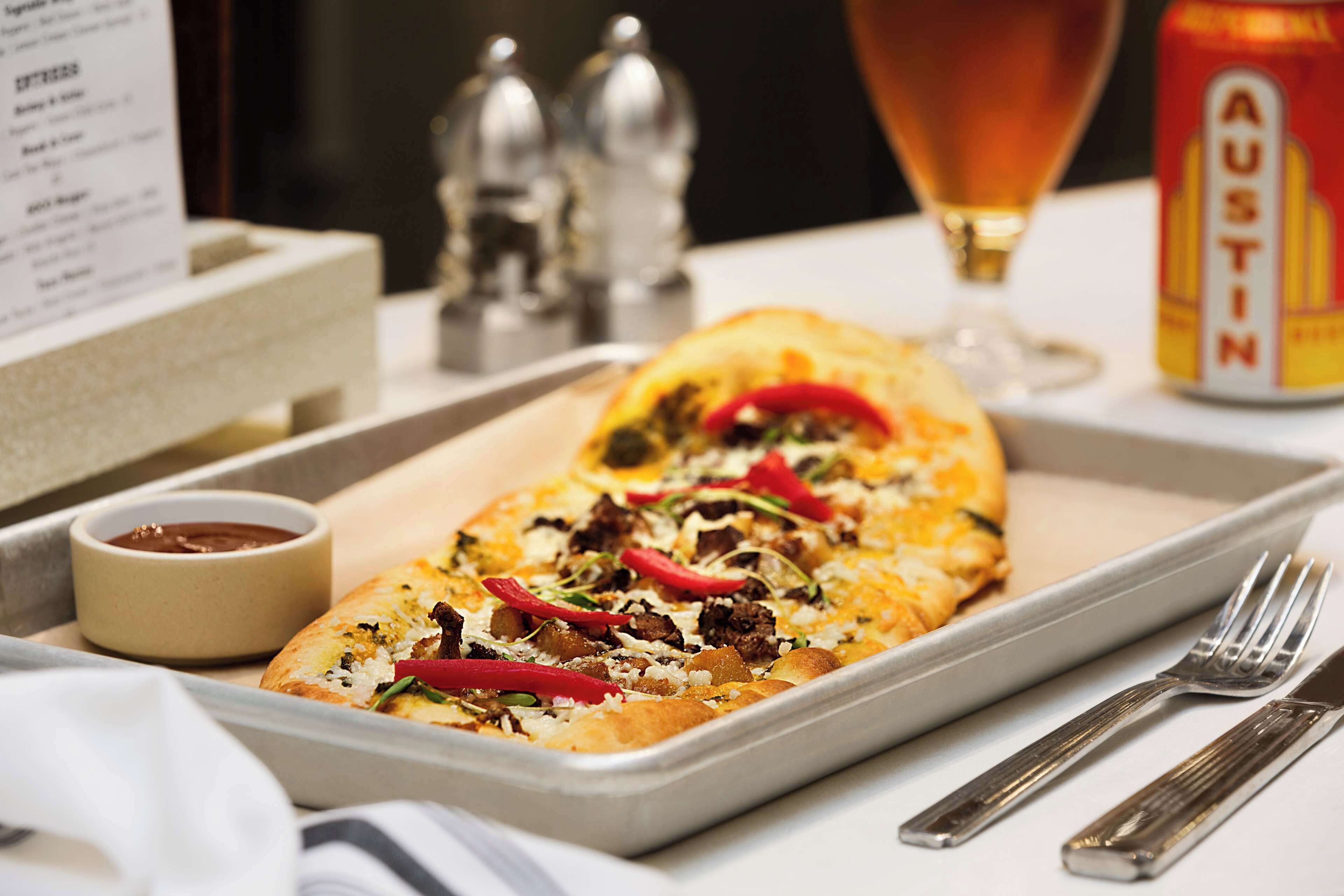 A tray with a pizza, a small bowl of sauce, and a can of Austin beer.