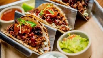 Three tacos with various toppings and sides including a bowl of guacamole and a small bowl of sauce.