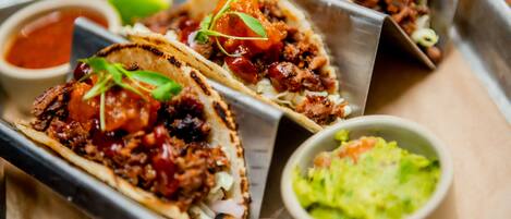 Three tacos with various toppings and sides including a bowl of guacamole and a small bowl of sauce.