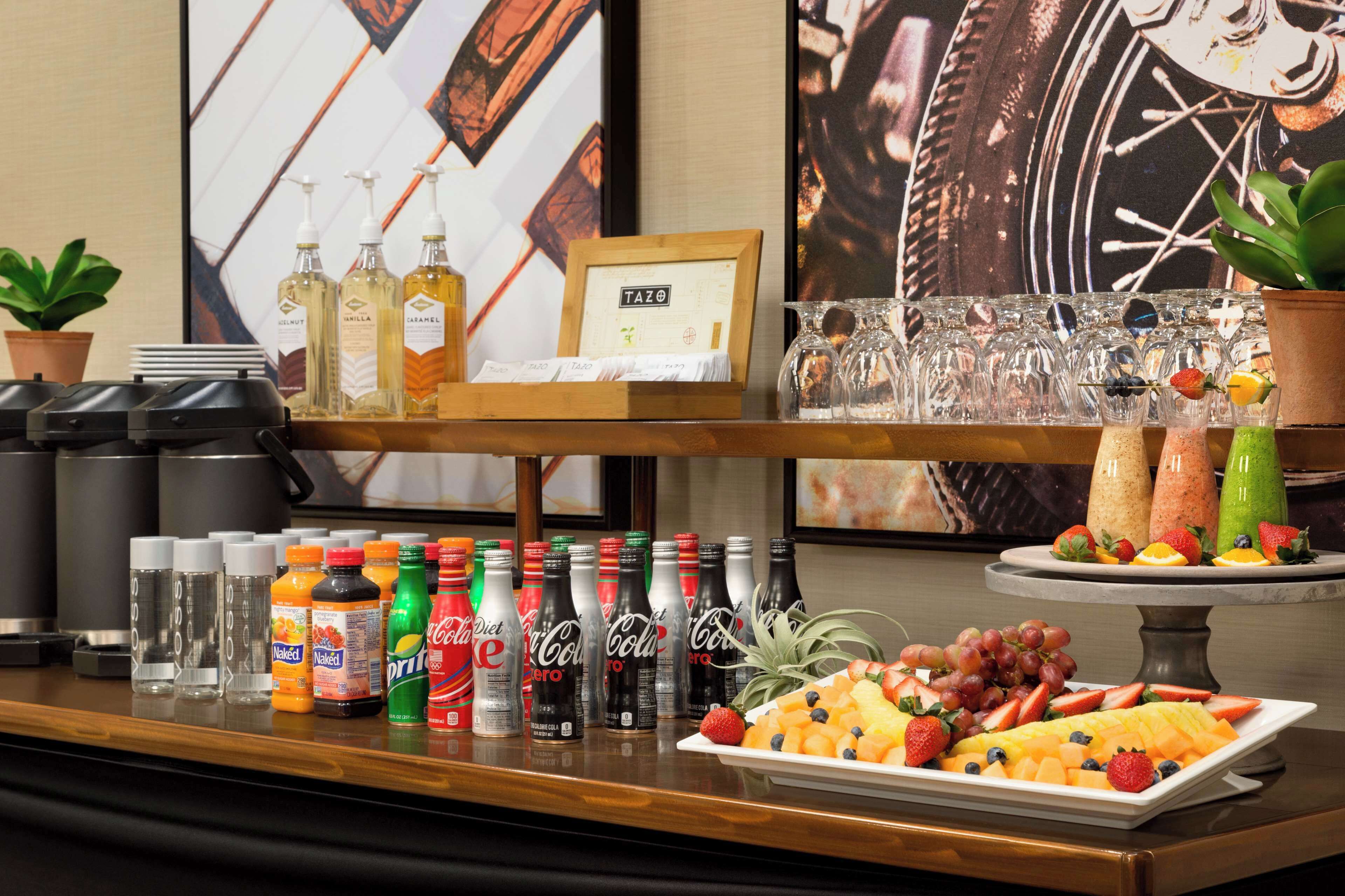 Una mesa de buffet con diversas bebidas, incluyendo Coca-Cola light y Coca-Cola regular, y una bandeja de frutas con fresas, uvas y piña.