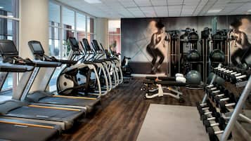 Academia com esteiras, aparelhos de musculação e um mural de uma figura musculosa.