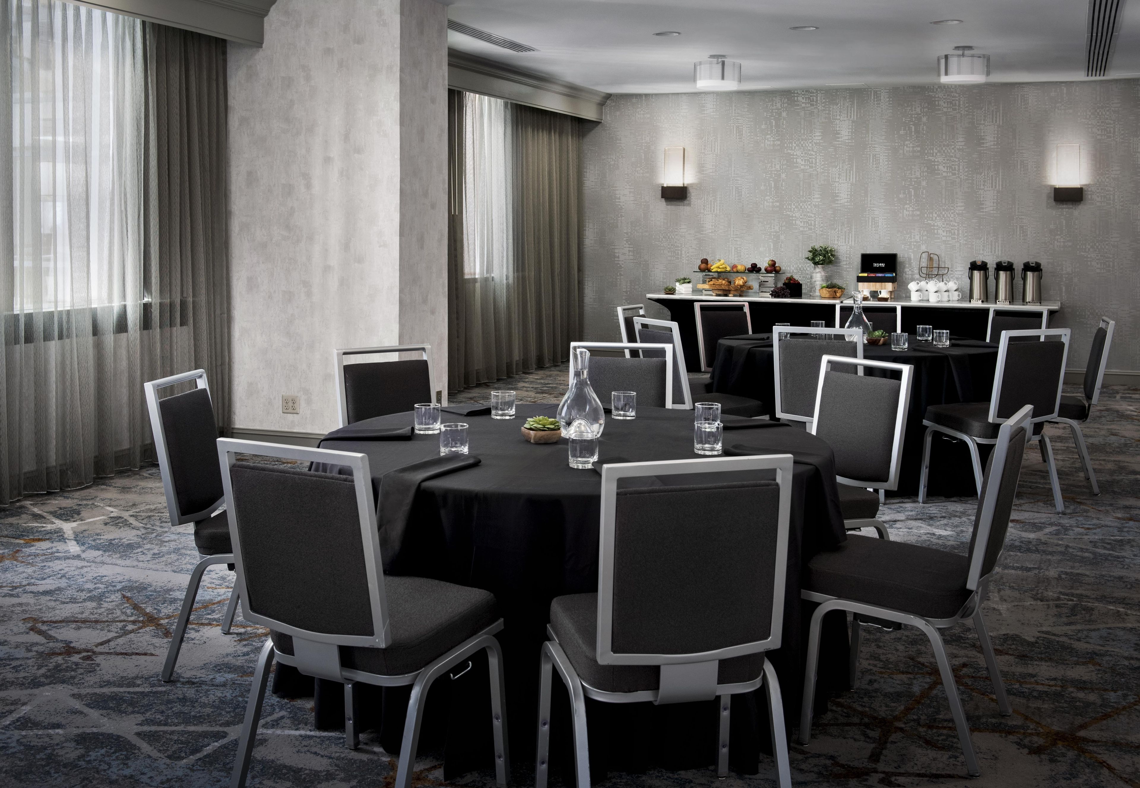 A conference room with round tables, chairs, and a buffet area with food and drinks.