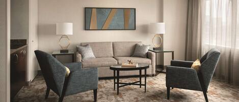 A modern living room with a beige sofa, two armchairs, a coffee table, and two lamps.