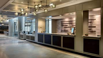 A modern reception area with a long counter, multiple seating areas, and a ceiling with spherical light fixtures.