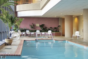A swimming pool with a tiled wall, lounge chairs, and potted plants.