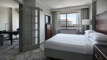 Une chambre d’hôtel comprenant un lit, un bureau, une chaise, une commode, un téléviseur, une fenêtre avec des rideaux et une lampe.