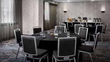 A conference room with round tables, chairs, and a buffet area with food and beverages.