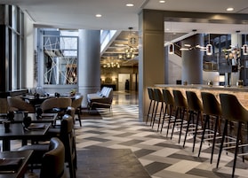 A modern hotel lobby with a bar area, seating arrangements, and a check-in counter.