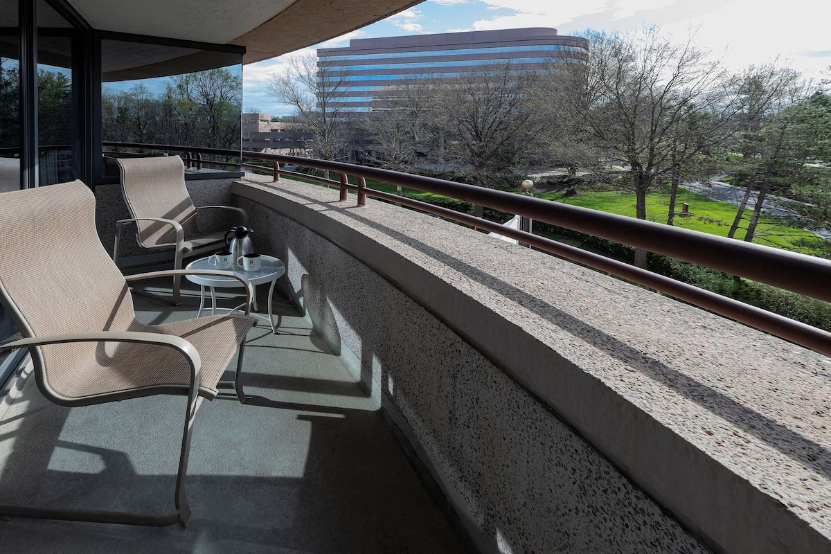 A balcony with outdoor seating, a coffee table, and a view of a building and trees.