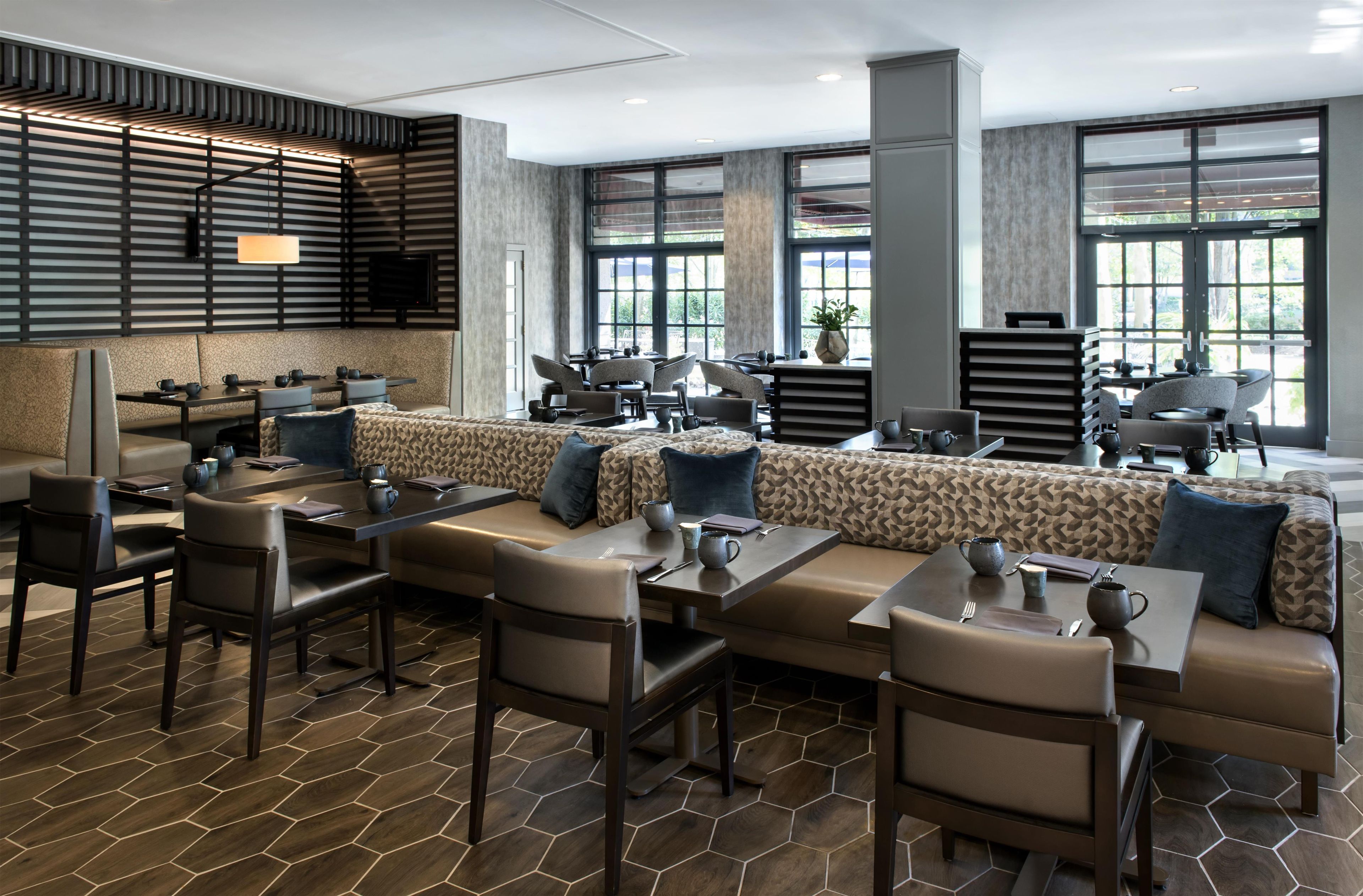 A modern restaurant with a long communal dining area, individual tables, and a variety of seating options.