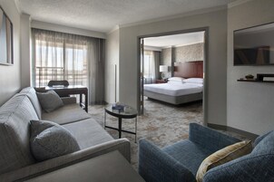 Una habitación de hotel con sofá, sillón, una pequeña mesa, cama y televisión.