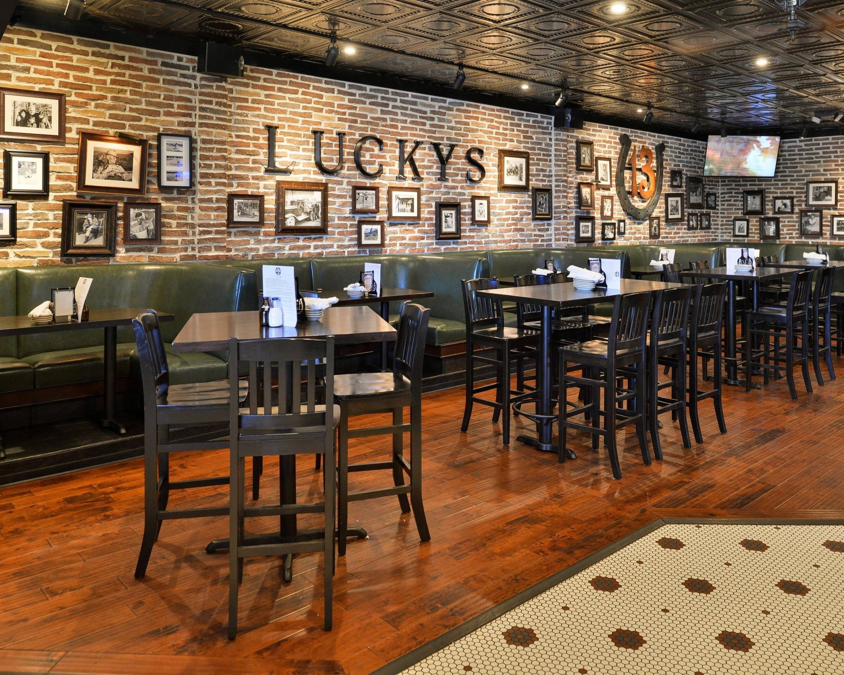 A restaurant interior with brick walls, framed pictures, and a large screen. Tables and chairs are arranged for dining.