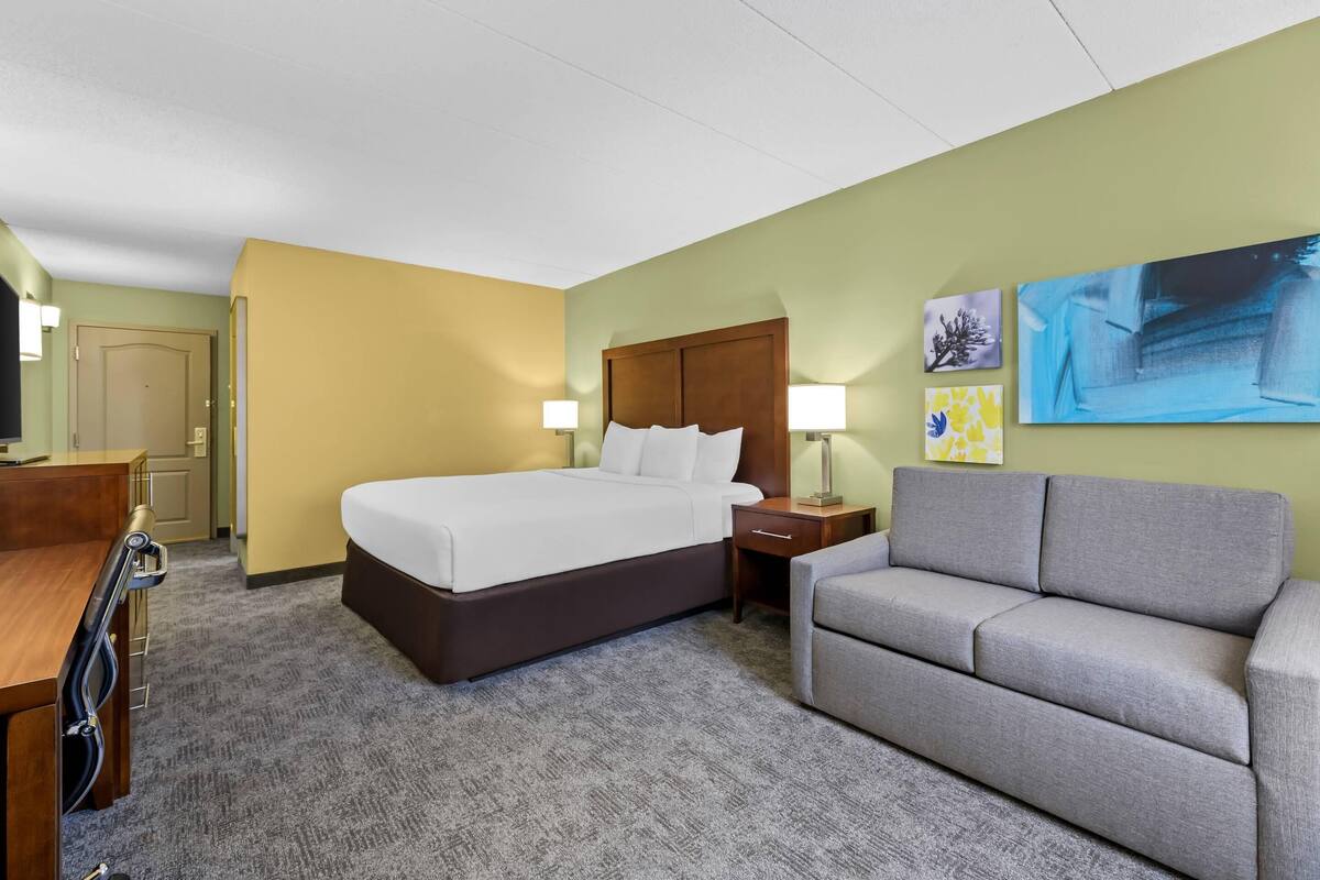 A hotel room with a bed, a sofa, a desk, and two wall-mounted lamps.