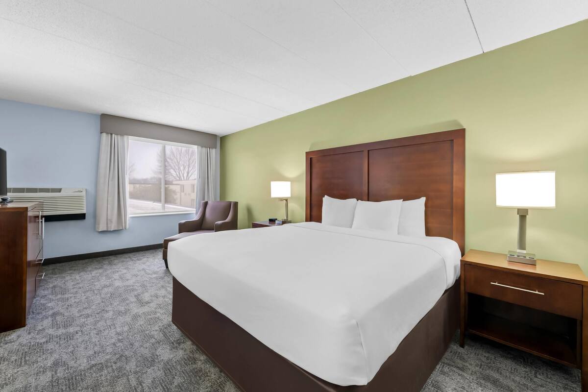 A hotel room with a large bed, two bedside tables, a chair, a desk, and a window with curtains.