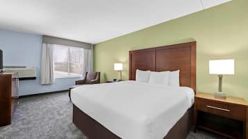 A hotel room with a large bed, two bedside tables, a chair, a desk, and a window with curtains.