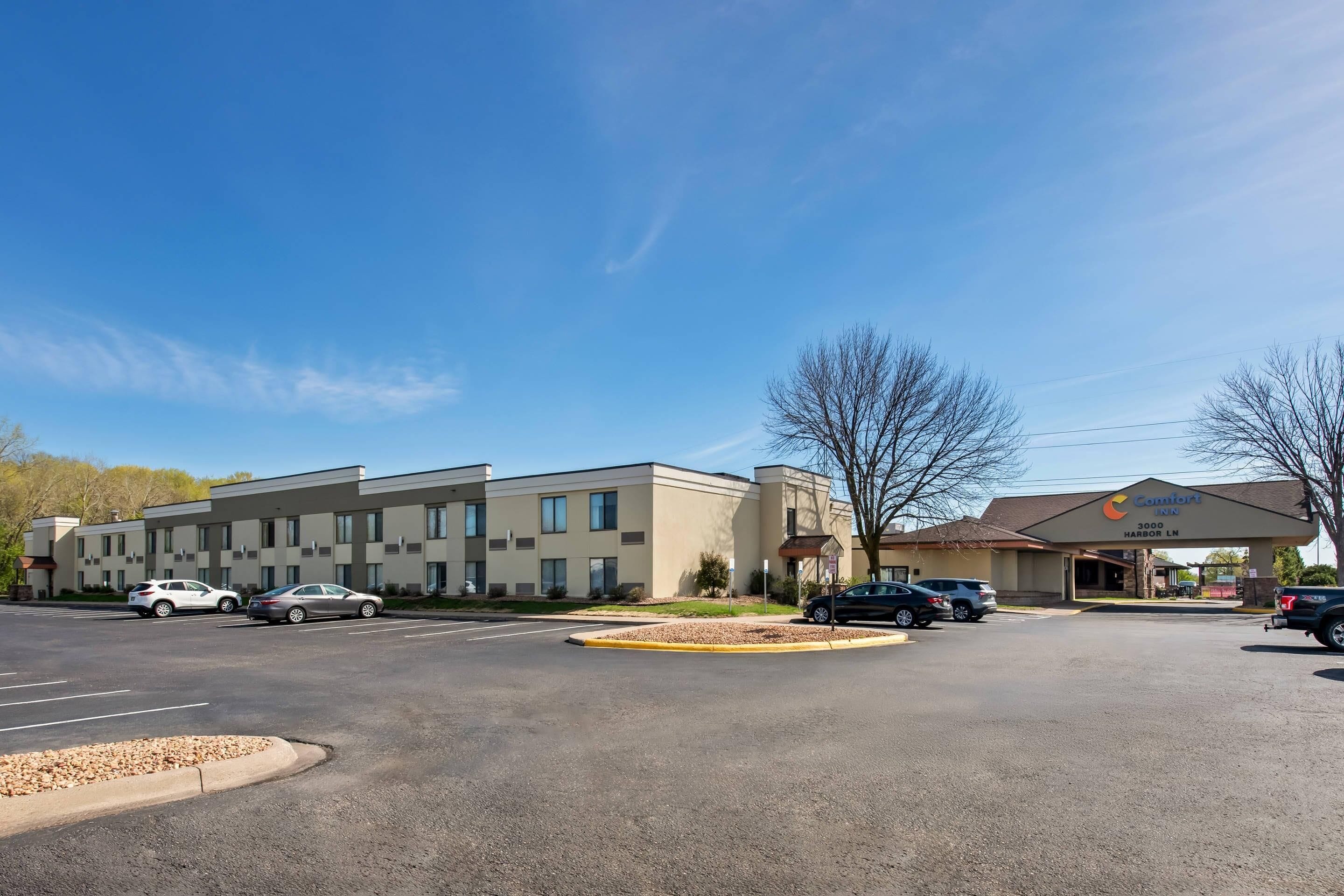 A multi-story hotel with a parking lot, a covered entrance, and a clear blue sky.