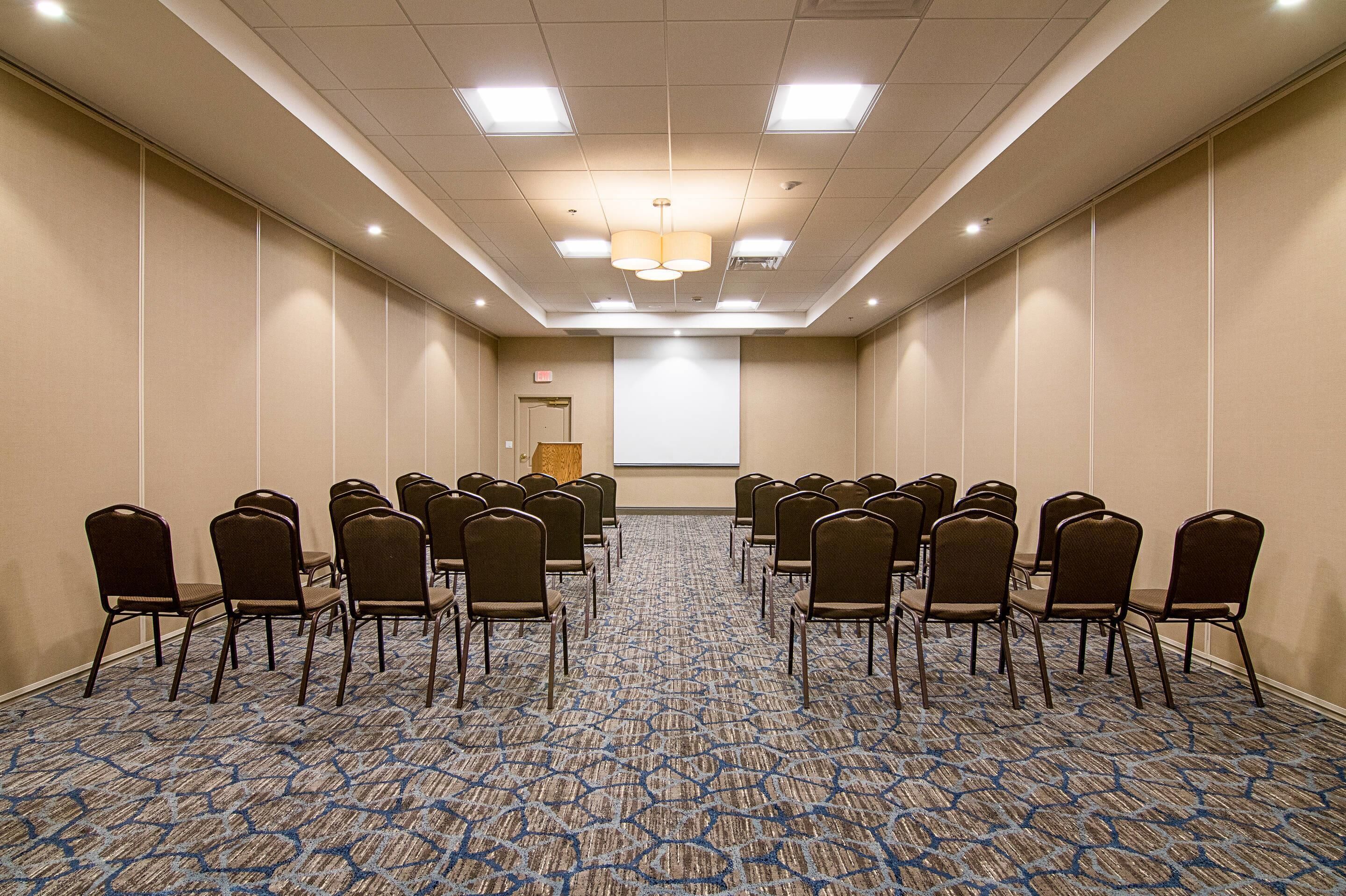 A conference room with rows of chairs, a projector screen, and a carpeted floor.