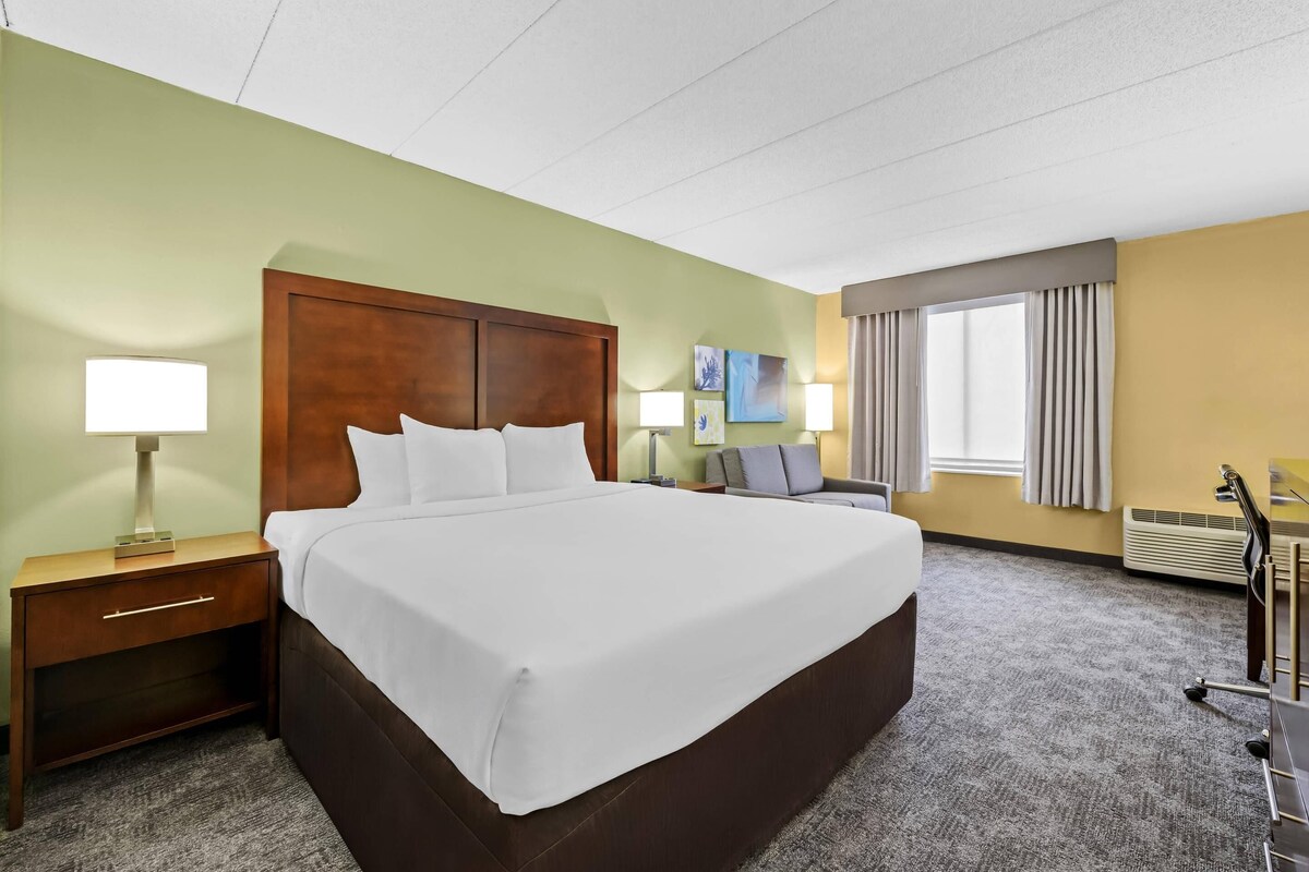 A hotel room with a large bed, a nightstand, a desk, and a chair.