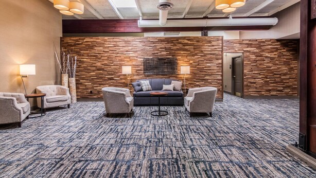 A lobby with a patterned carpet, a sofa, armchairs, a small table, and wall-mounted lamps. - Comfort Inn Plymouth - Minneapolis (Plymouth)