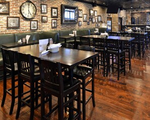 A restaurant with brick walls, framed pictures, a clock, wooden tables, and green booths.
