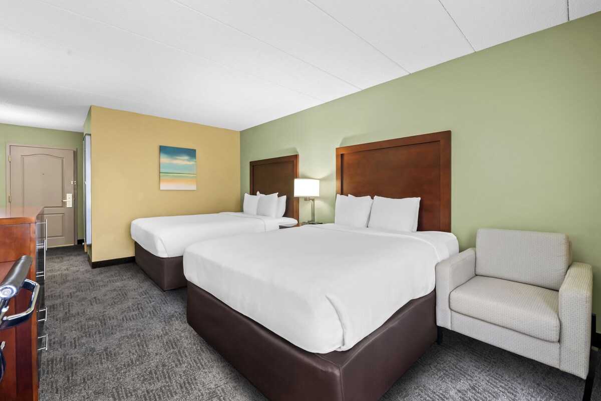 A hotel room with two beds, a chair, a desk, and a lamp.