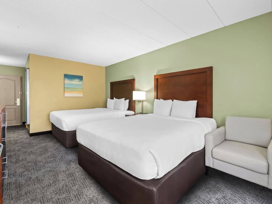A hotel room with two beds, a chair, a desk, and a lamp.