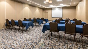 A conference room with multiple tables and chairs, a carpeted floor, and a projector screen on the wall. - Comfort Inn Plymouth - Minneapolis (Plymouth)