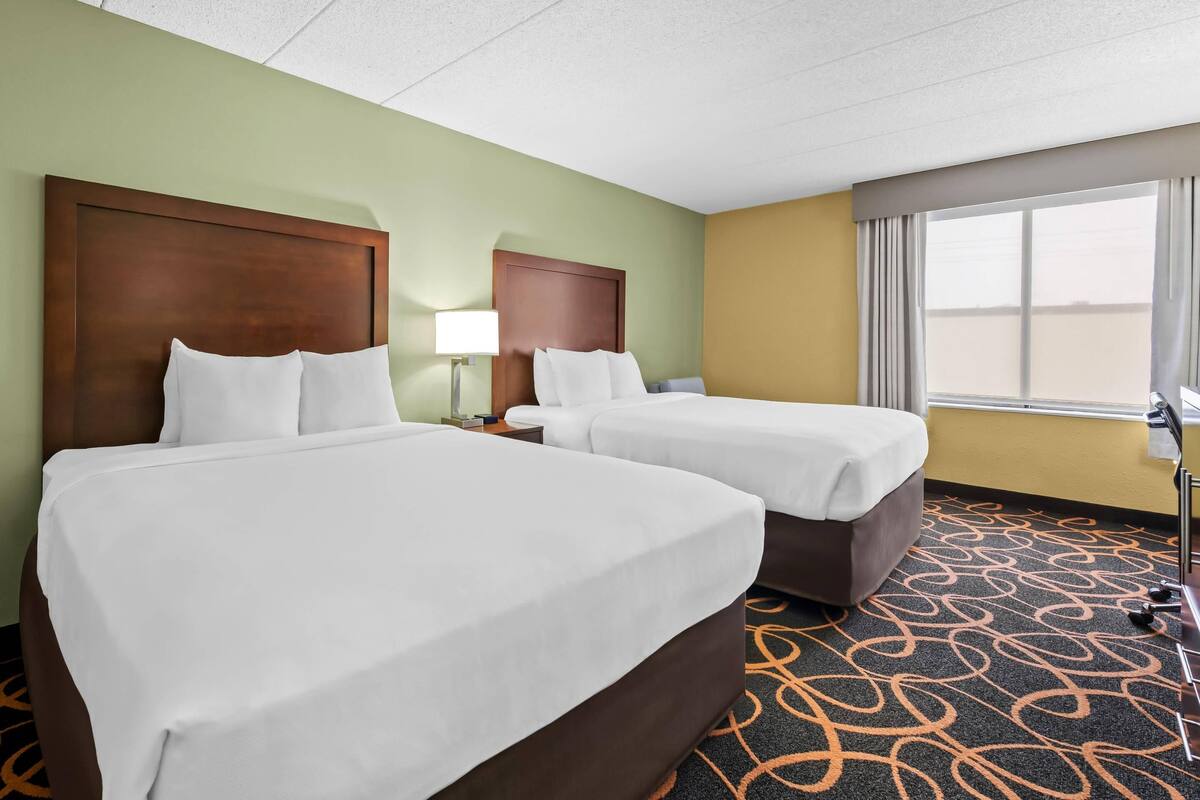 A hotel room with two beds, a window with curtains, a lamp, and a patterned carpet.