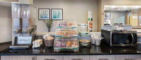 A hotel breakfast area with a coffee machine, snack dispensers, and a microwave.