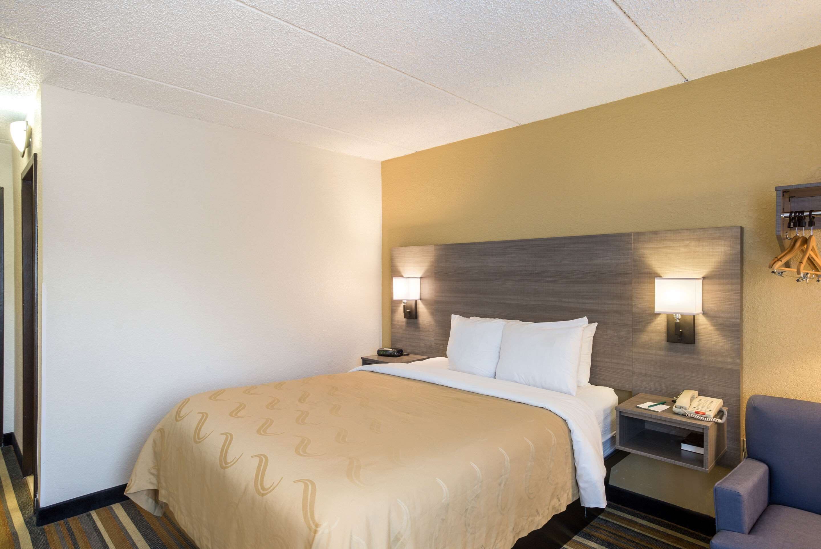 Una habitación de hotel con cama, lámparas de noche, mesita de noche y una silla.
