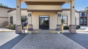A hotel entrance with a covered walkway, potted plants, and a brick-paved driveway. - Quality Inn Albany Colonie (Albany)