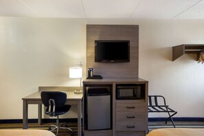 A hotel room with a desk, chair, television, refrigerator, and a bed.