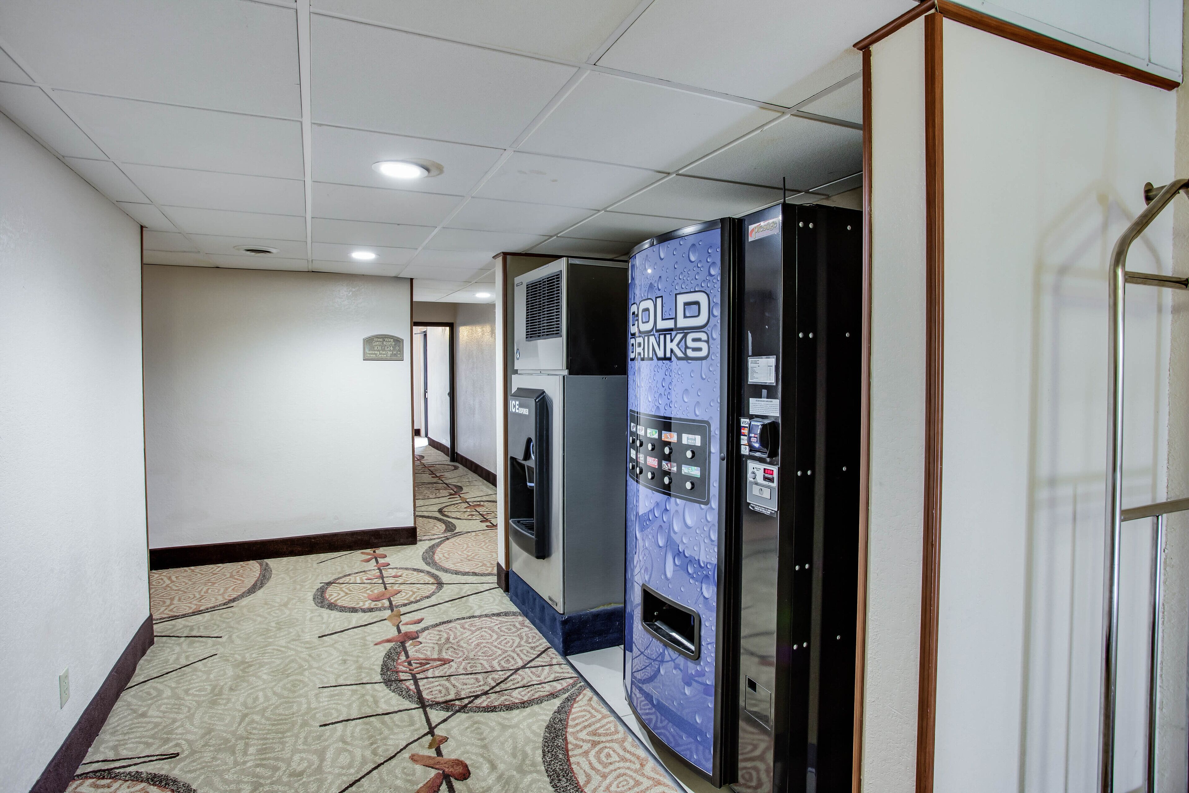 A hotel corridor with a patterned carpet, vending machines labeled "Cold Drinks," and a door with a metal handle.