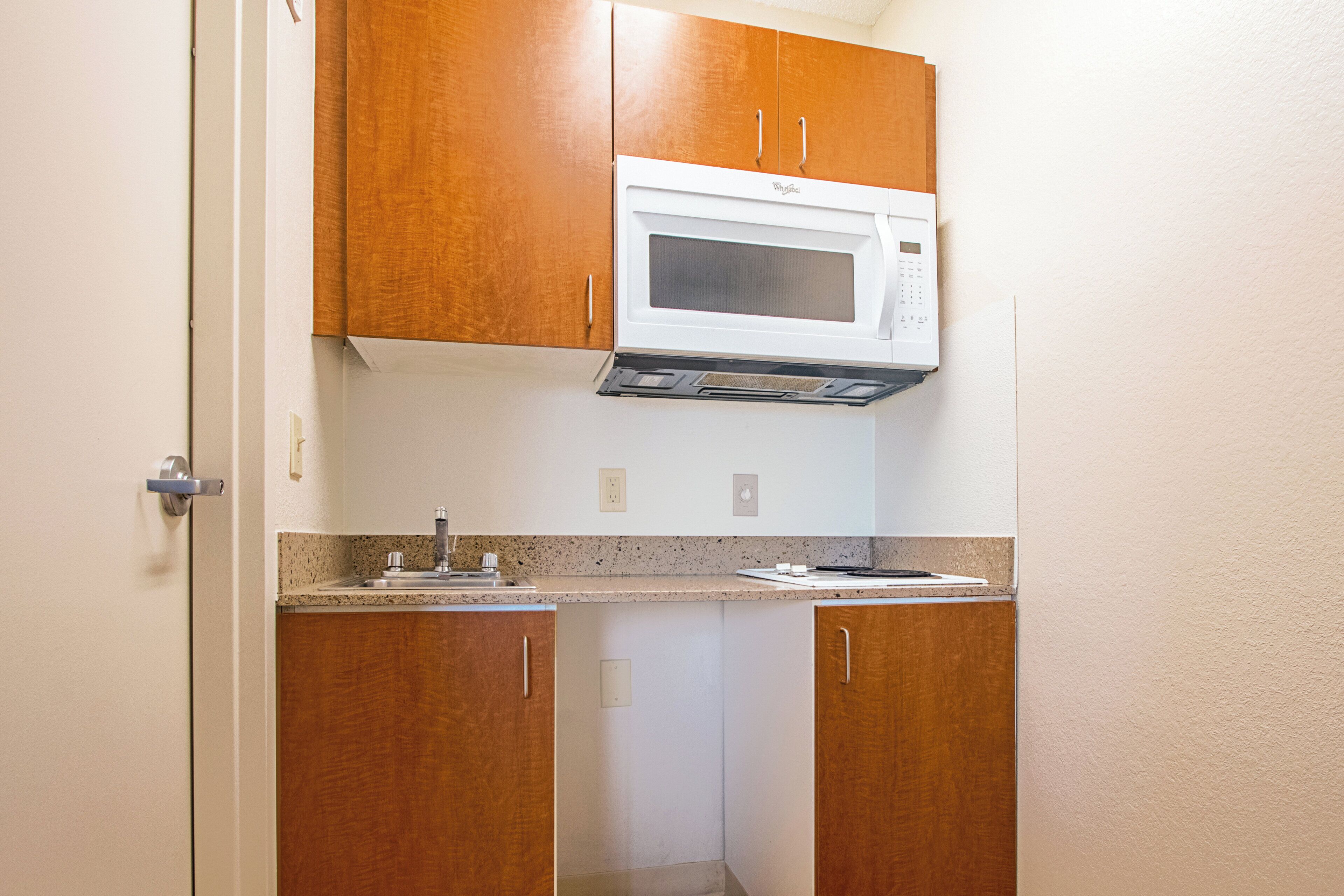 A compact kitchen with wooden cabinets, a built-in microwave, and a stainless steel sink.
