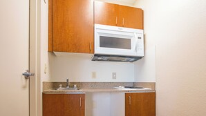 Una cocina compacta con armarios de madera, un microondas integrado y un lavamanos de acero inoxidable.