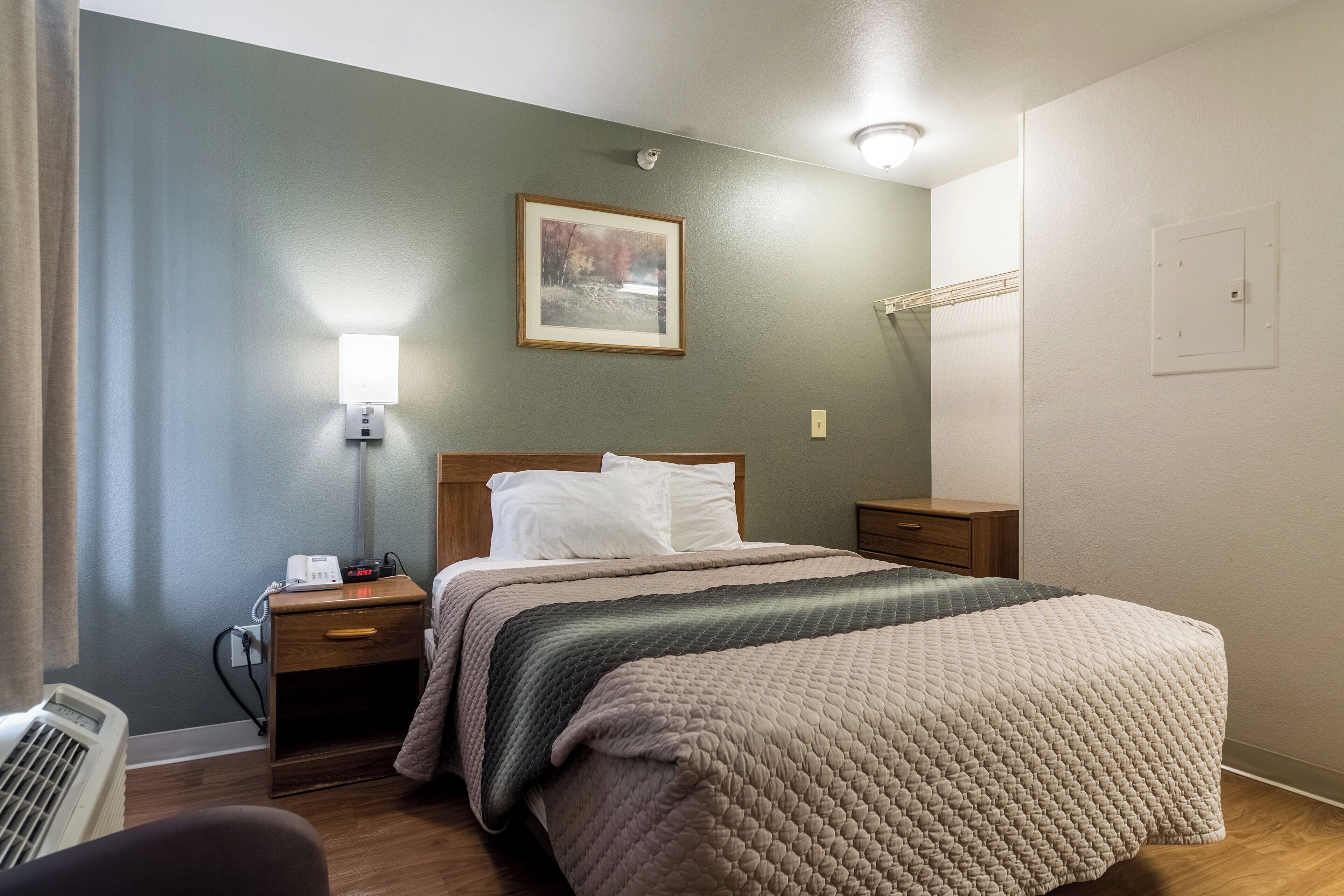 Una habitación de hotel con cama, mesitas de noche, lámpara, un cuadro y un enchufe.