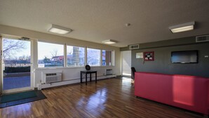 Una habitación con ventanas amplias, un banco rojo, una mesita y un televisor instalado en la pared.