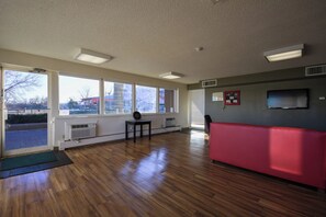 A room with large windows, a red bench, a small table, and a wall-mounted TV.