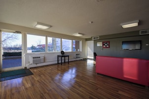 Una habitación con ventanas amplias, un banco rojo, una mesita y un televisor instalado en la pared.