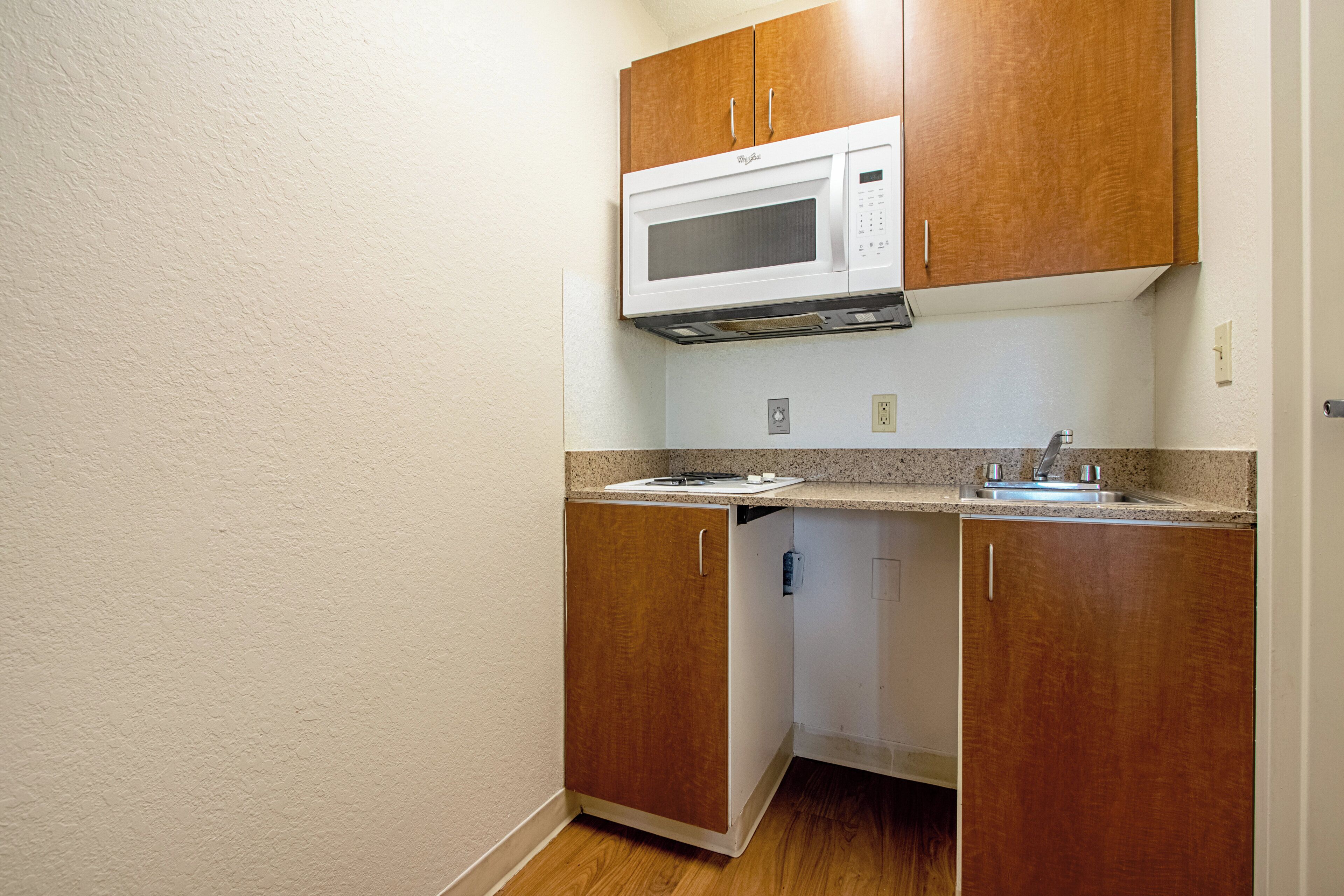 Cocina compacta con armarios de madera, microondas integrado y encimera de granito.