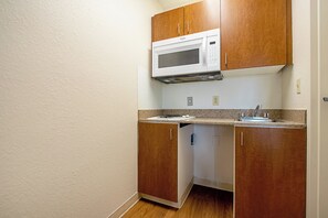 A compact kitchen with wooden cabinets, a built-in microwave, and a granite countertop. - HomeTowne Studios by Red Roof Denver - Lakewood West (Lakewood)