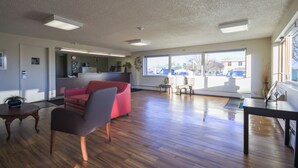 A spacious living area with a red sofa, a small table, and a view of the parking lot through large windows.