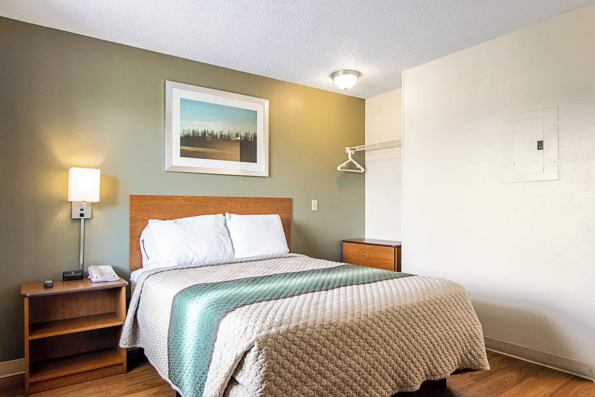 Une chambre d’hôtel avec un lit, une table de chevet, une lampe et un tableau encadré au mur.