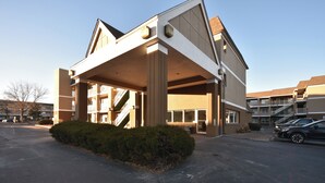 A building with a covered entrance, a staircase, and a parking lot.