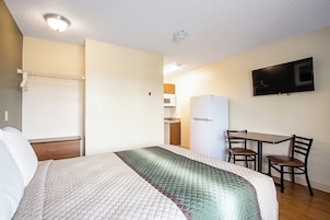 Una habitación de hotel con cama, escritorio, silla, televisión y kitchenette.