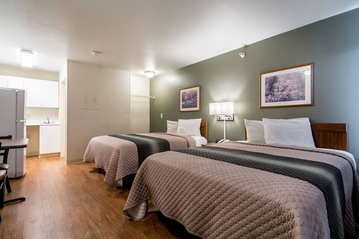 Ein Hotelzimmer mit zwei Betten, einem Schreibtisch, einem Stuhl, einer Lampe und Bildern an den Wänden.