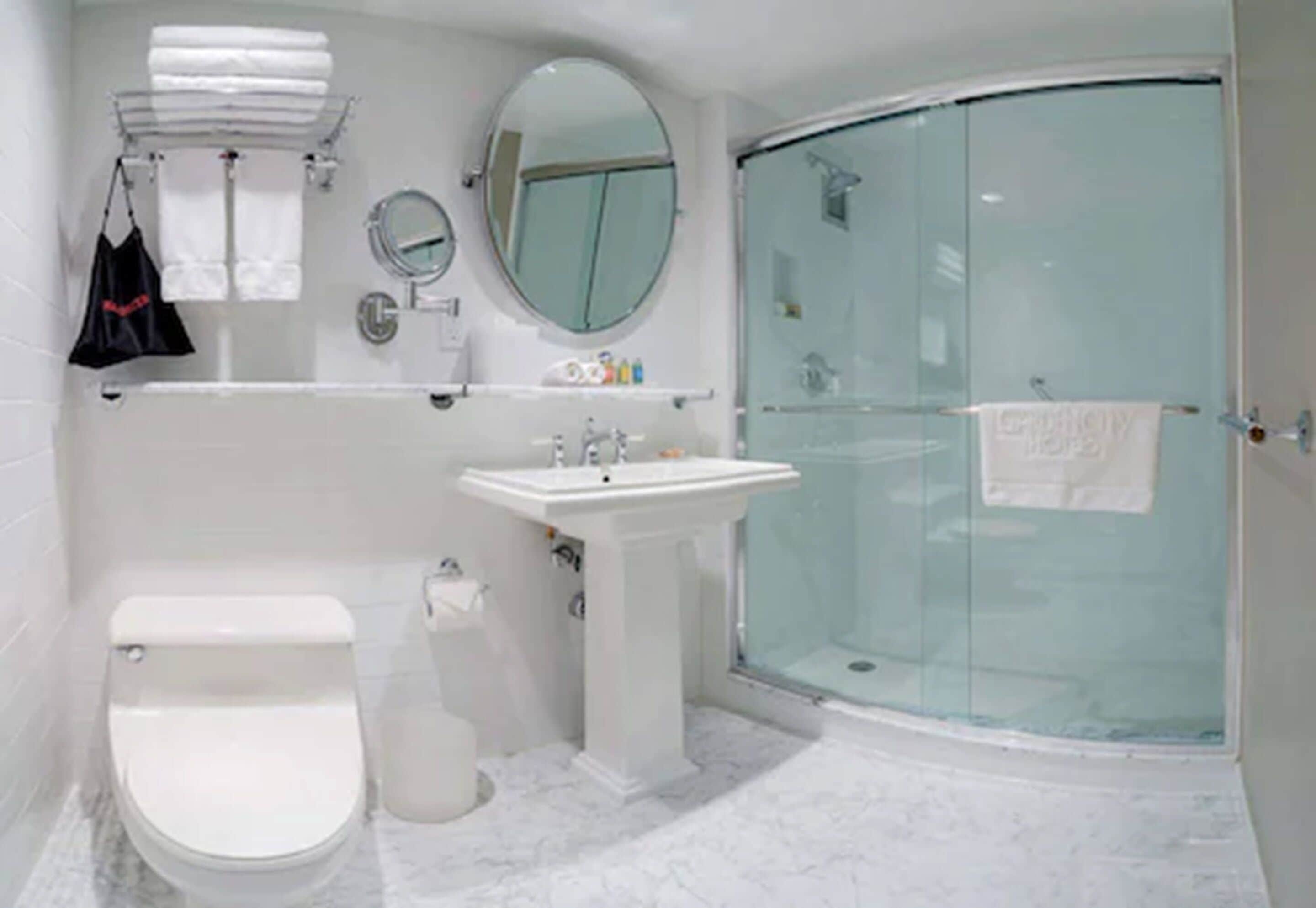 A bathroom with a toilet, sink, mirror, and glass shower enclosure.