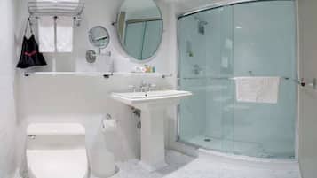 A bathroom with a toilet, sink, mirror, and glass shower enclosure.