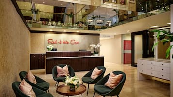 Der Rezeptionsbereich von Red Hot Spa zeichnet sich durch ein modernes Design aus, inklusive einer Rezeption, einer Sitzecke mit Stühlen und einem Glasgeländer mit Blick auf die Lobby.