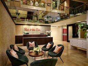 A Red Hot Spa reception area with a modern design, including a reception desk, seating area with chairs, and a glass railing overlooking the lobby. - The Garden City Hotel (Garden City)